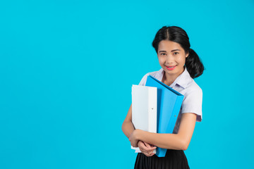 Obraz premium An Asian student girl holding her work file on a blue background.