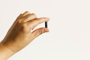 Dietary supplements. Hand holding spirulina capsule on white wall background. Morning vitamin nutrient pill. Health support and treatment. Biologically active additives
