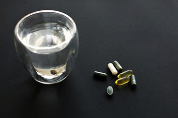 Dietary supplements. Omega 3, spirulina, chlorophyll,magnesium  capsules and water glass on black dark background. Morning vitamin pills. Health support and treatment.