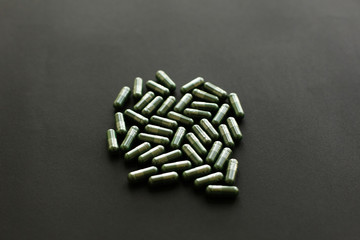 Spirulina capsules on black dark background. Dietary supplements. Health support and treatment, wellbeing. Biologically active additives. Vegan detox pills