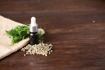 Hemp oil, which is paired with hemp leaves and seeds on a brown wooden floor.