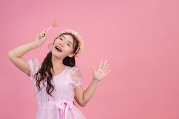 A beautiful woman dressed in a pink princess is playing with her sweet candy on a pink background.