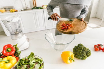 cropped view of woman putting cherry tomatoes in glass bowl