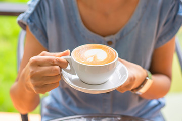 Hands holding white coffee cup with saucer.