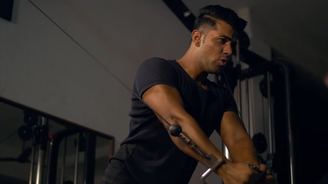 Handsome muscular North Indian young man working out on a cable machine in his home gym. 
