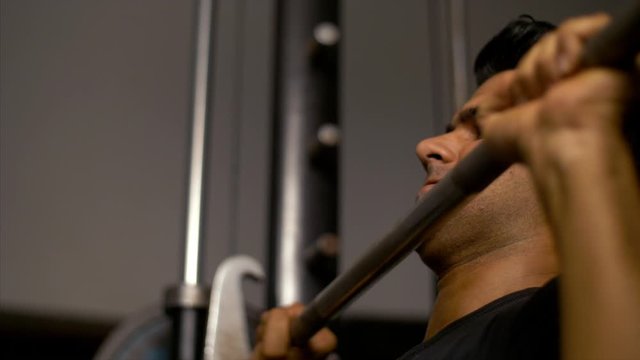 Fit young Indian athlete doing workout and lifting barbell in the gym. 