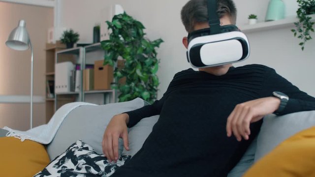 Young man in living room seat on sofa with virtual reality 3d glasses. Creative future concept. Man online relaxing or work in home.