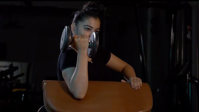 Young female athlete working out with dumbbells in gym. 