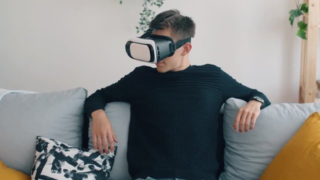 Young man in living room seat on sofa with virtual reality 3d glasses. Creative future concept. Man online relaxing or work in home.