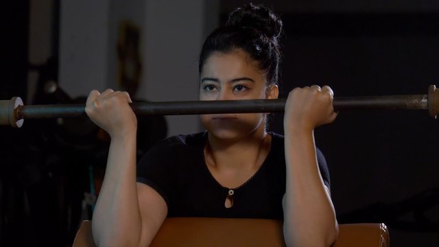 Fit young Indian girl doing bicep exercise with weights in the gym. 