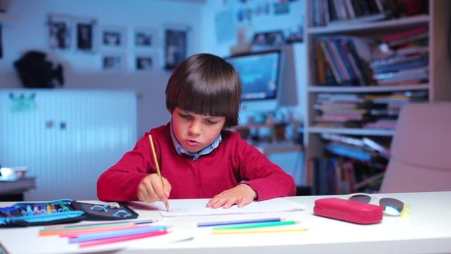 a boy sits at a table, draws a picture