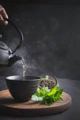 Pour hot tea with steam into cup on black table. Chinese tea.