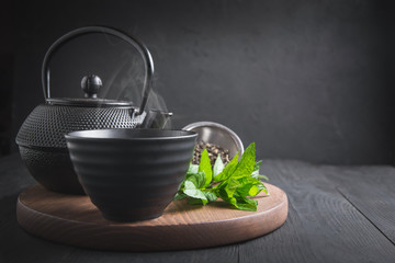 Cup tea with mint and kettle on dark background. Chinese tea concept.
