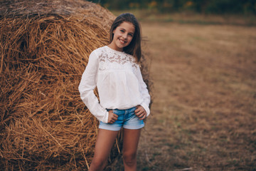 Little girl in a field with hay rolls at sunset