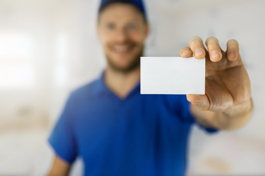 smiling handyman in blue uniform showing blank business card