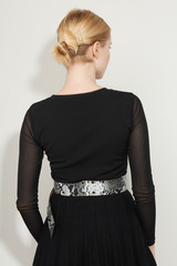 Cropped back view shot of a blond girl, posing on a white background. She is wearing black gown with transparent sleeves and grey snake print wide belt with holes on it. 