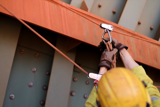 Closeup picture of male rope access worker hand wearing safety glove checking inspecting Karabiner which clipping on the tie line prior abseiling working at height construction site, Sydney, Australia