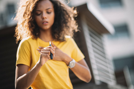 Afro girl smoking e-cigarette and coughing