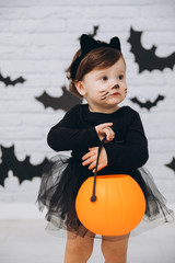 A little girl in a black cat costume with a pumpkin basket on a bats background, trick or treat, Halloween concept.