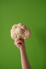 Female hand holds cauliflower on a green background. The concept of veganism and vegetarianism. © Oleg Samoylov