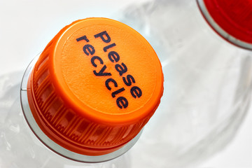 Plastic bottles and orange and red bottle caps with please recycle message against a white background. Concept of plastic pollution.	