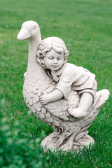 Fototapeta na wymiar Garden figurine on green grass. Statuette of a girl on a goose.
