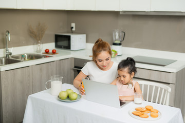 Happy Asian family are eating breakfast and see digital tablet in the kitchen at home. Healthy food and Morning activities