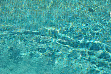 Mosaic bottom through the transparent water with spots of light in the pool
