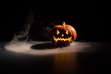 Halloween, orange pumpkin with a scary luminous face on a dark background. Gray thick smoke comes...