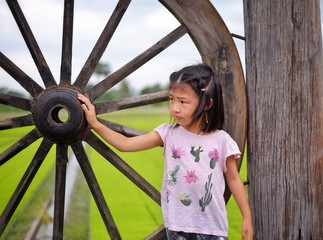 A cute Thai girl standing next to an old wooden wheel at a rice field in rural Thailand.