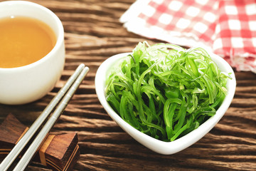 Hiyashi Wakame Chuka or seaweed salad in white bowl leaf with stainless steel chopsticks and teacup on wooden table, Japanese food