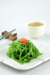 Hiyashi Wakame Chuka or seaweed salad in white bowl with stainless steel chopsticks and teacup on white background, Japanese food