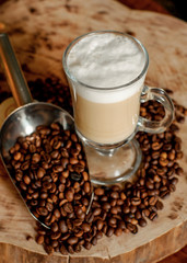 Latte coffee. Coffee with milk. Cappuccino in a glass cup on a wooden table. Cappuccino coffee and roasted coffee beans.