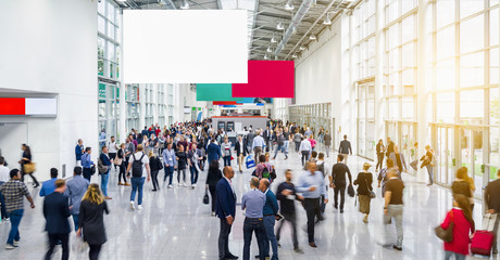 Many anonymous people are walking around advertising banner at a trade fair, copyspace for your individual text.