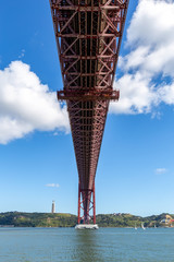 Under the bridge, calm river with sailing boats and a statue on top of the hill