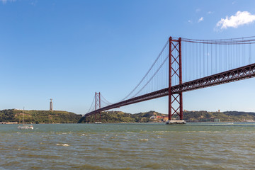 River side with red bridge and a statue on top of the hill