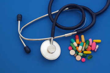 Stethoscope and drugs and pills on blue background, pharmaceutical concept 