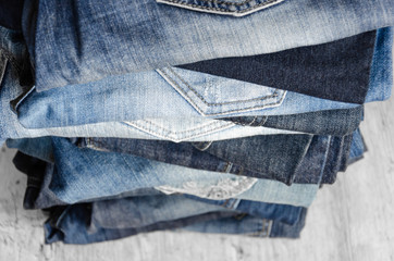 A stack of carelessly folded woman's jeans on gray background. Close-up of jeans in different...