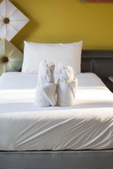 Two white hotel towels on white single bead with one pillow and yellow wall