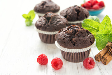 Chocolate muffins with raspberries and mint leaves on white table