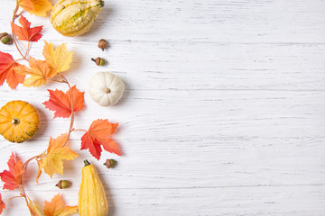Autumn leaves and mini pumpkins over white wooden background, copy space, top view