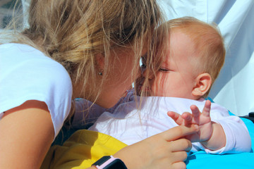 People, childhood, family concept. Cropped shot of a cute baby girl over blue sky background. Sisters hugs, close up. The older sister kisses the younger sister.