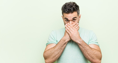 Young handsome man against a green background shocked covering mouth with hands.