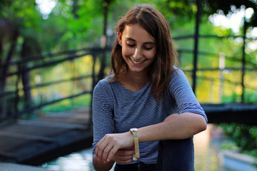 Young and beautiful girl dressed in gray putting on a gold and quartz watch.  Girl with gold...