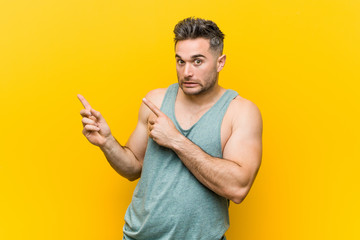 Young fitness man against a yellow background shocked pointing with index fingers to a copy space.