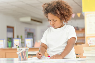 Mix Asian and African little toddler girl concentrate drawing in library. Child drawing on free...