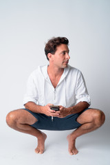 Full body shot of handsome Hispanic man crouching and thinking while using phone