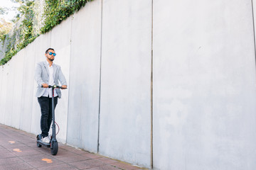 Latin adult man with sunglasses, well dressed and electric scooter on the street with a white blind background