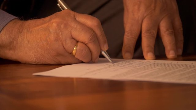 Senior man signing a legal document with a pen . Indian stock footage of a senior man filling and signing his legal will papers