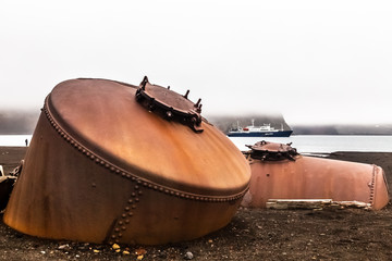 Abandoned norwegian whale hunter station rusty blubber tanks with cruise vessel in the bay , at...